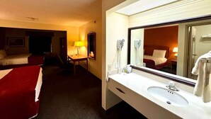 A hotel room with a bed, a desk, a lamp, a phone, and a bathroom with a sink and mirror.