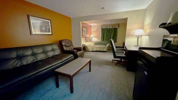 A hotel room with a leather sofa, a small table, a desk with a lamp, a bed with a green curtain, and a framed picture on the wall.