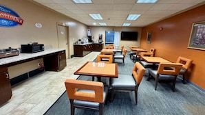 A restaurant with multiple tables and chairs, a counter with a coffee machine, and a television on the wall.