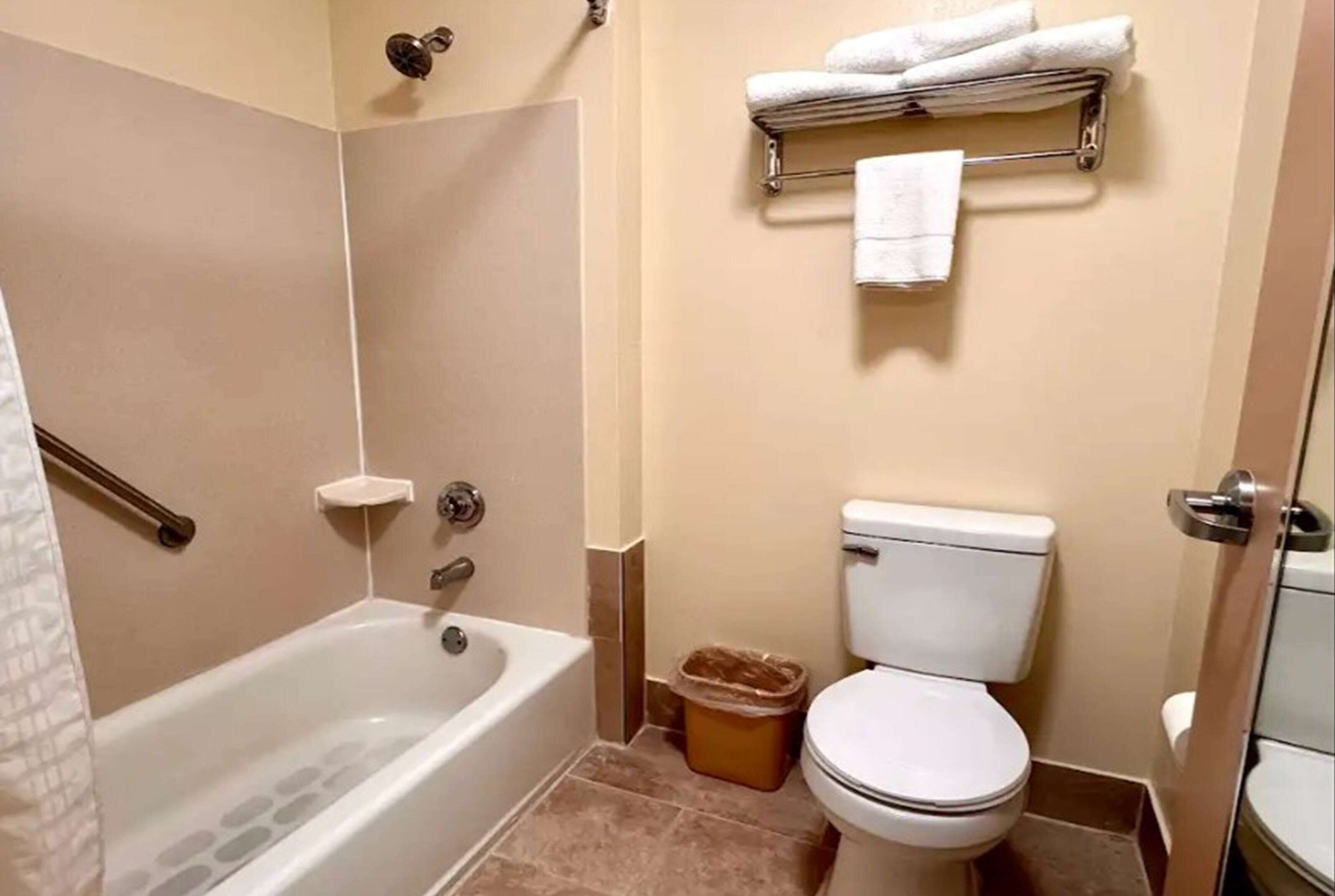 A bathroom with a bathtub, toilet, and a towel rack with towels.
