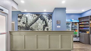 A reception area with a counter, a wall-mounted artwork, a refrigerator stocked with beverages, and shelves with snacks. - Best Western Chambersburg (Chambersburg)
