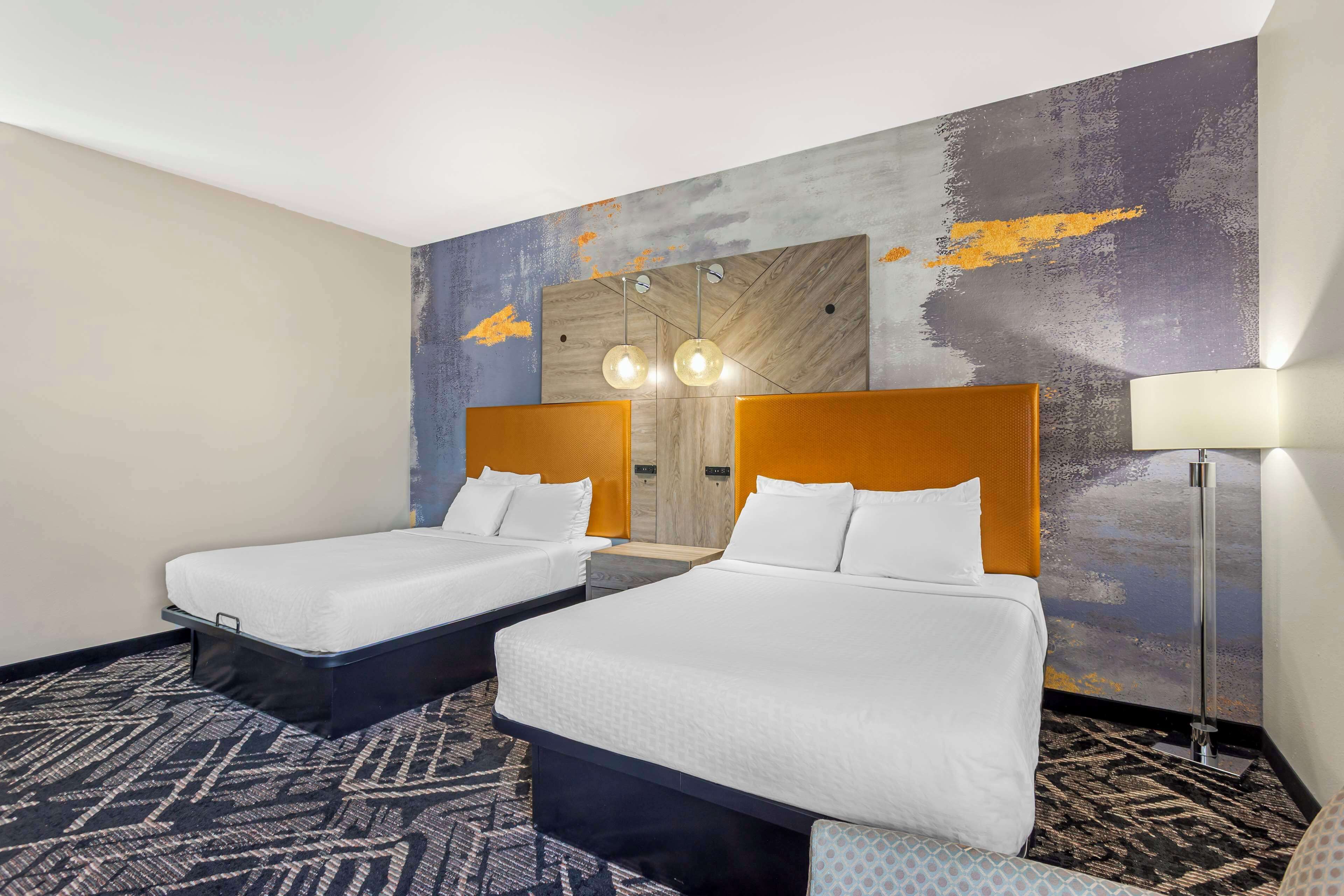 Een hotelkamer met twee bedden, een grote spiegel en een vloerlamp.