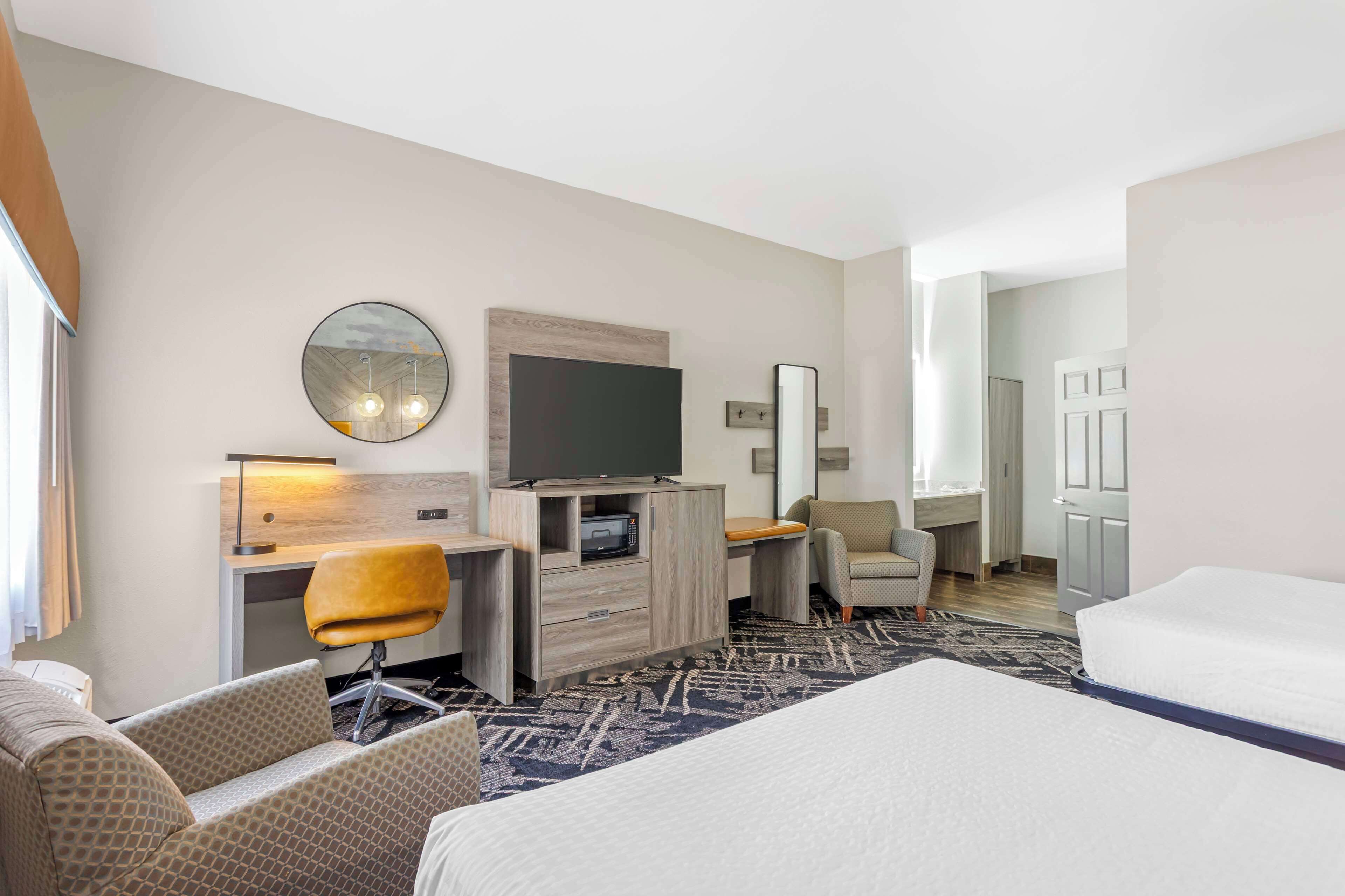 A hotel room with a large bed, a desk with a flat-screen TV, a chair, and a sofa.