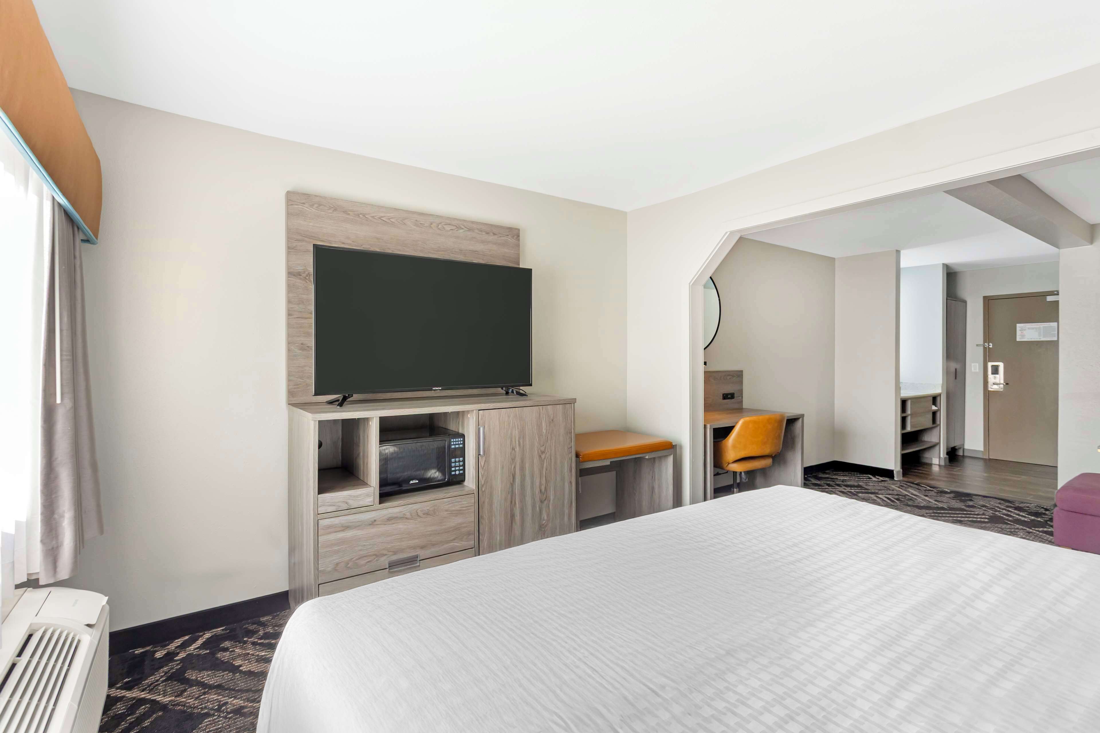A hotel room with a large bed, a flat-screen TV mounted on a wooden cabinet, a desk with a chair, and a small seating area.