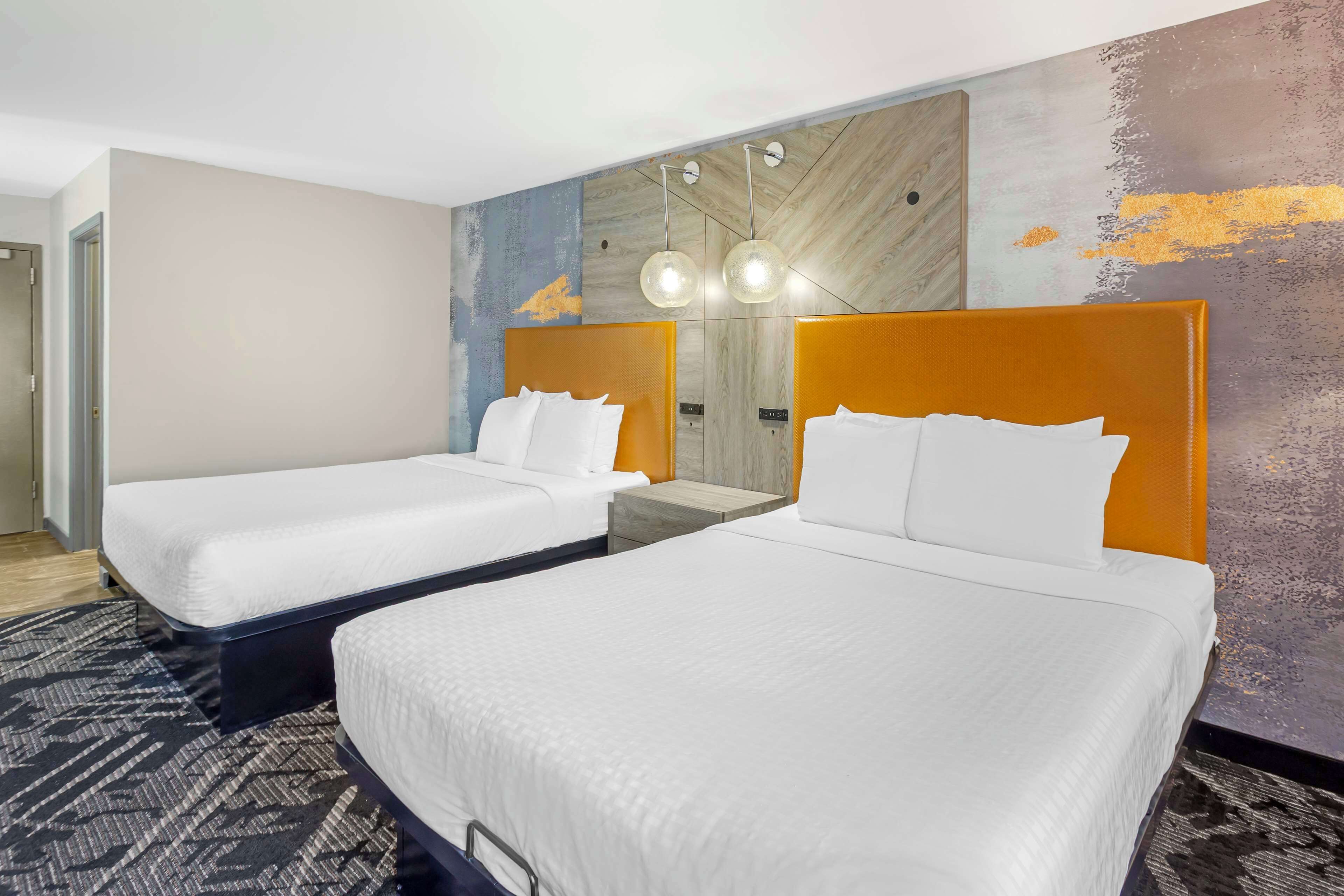 A hotel room with two beds, a modern wall design, and a patterned carpet.