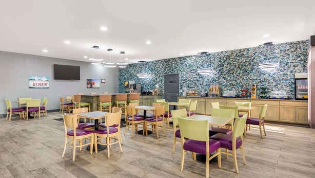 A modern dining area with wooden tables and chairs, a kitchen in the background, and a 'DINER' sign on the wall. - Best Western Chambersburg (Chambersburg)