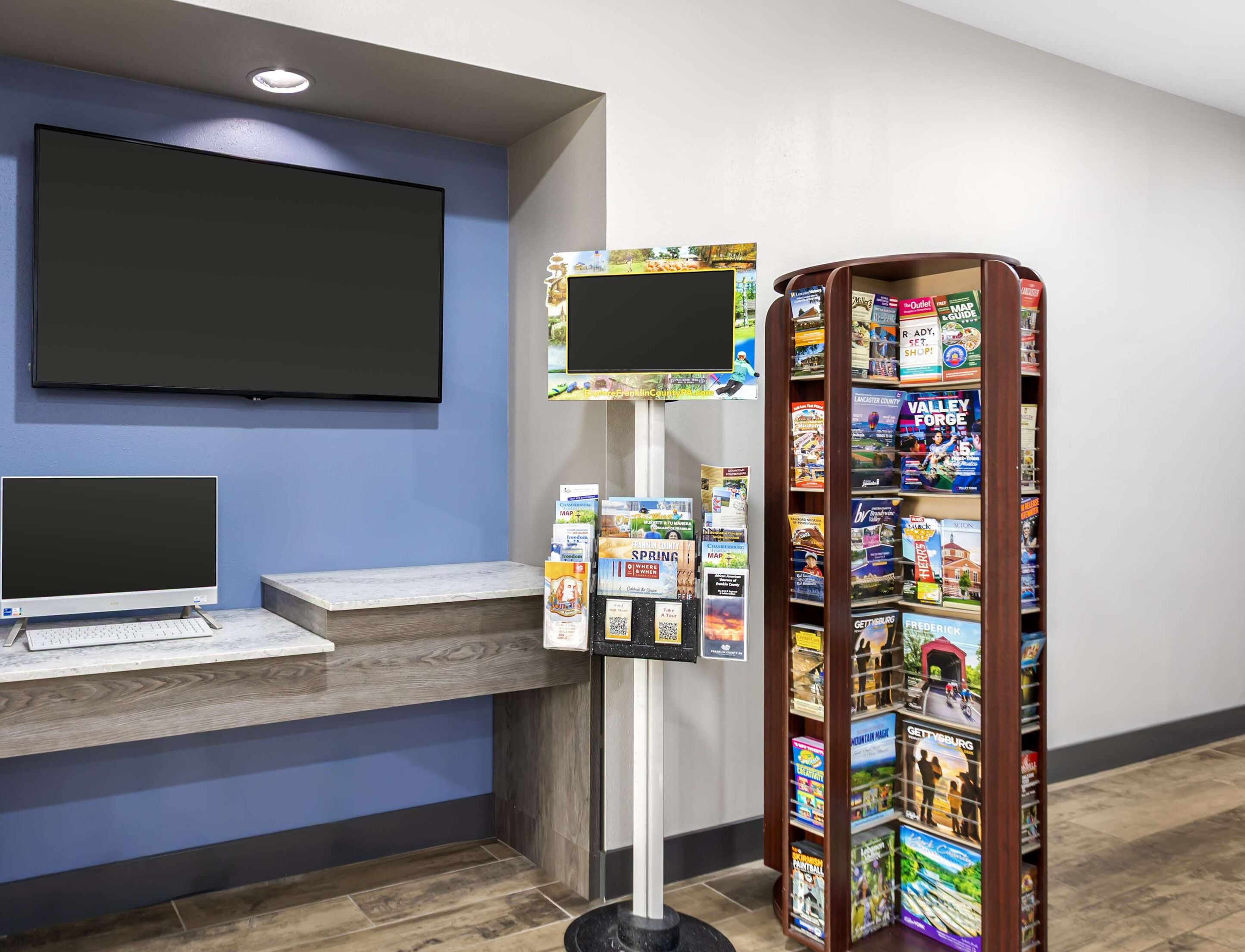 Un espace d’accueil équipé d’un écran plat, d’un ordinateur, d’un terminal en libre-service et d’un présentoir à magazines.