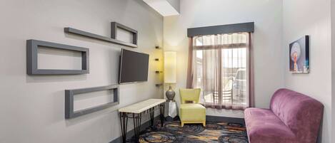 A hotel room with a TV, a desk, a chair, a sofa, and a patterned carpet.