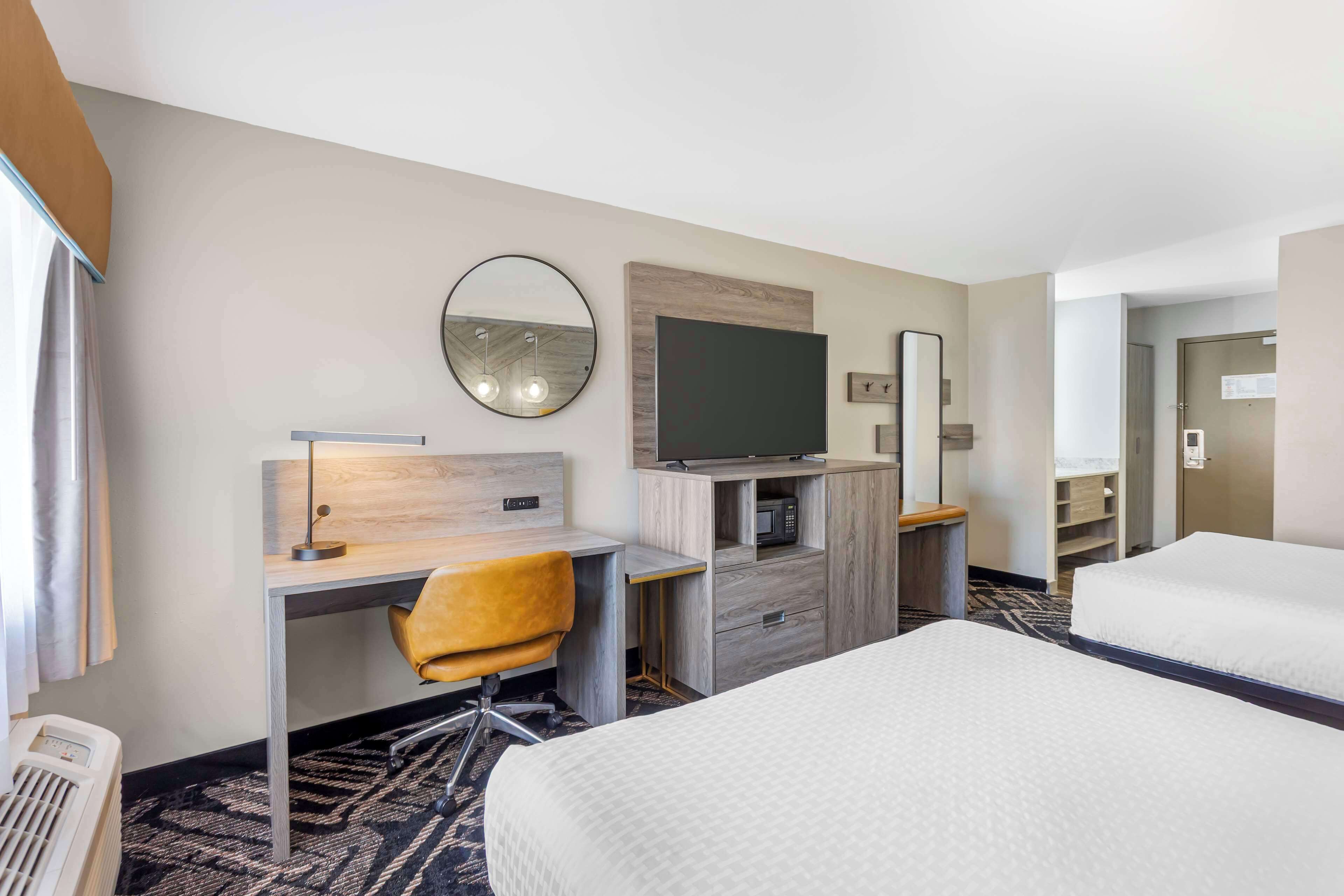 Een hotelkamer met een bed, een bureau met stoel, een televisie, een spiegel en een magnetron.