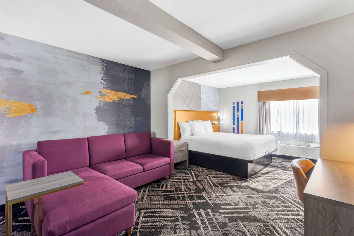 A hotel room with a large bed, a sofa, a small table, and a patterned rug.