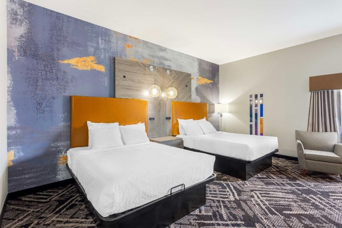 A hotel room with two beds, a sofa, a wall with abstract art, and a patterned carpet.