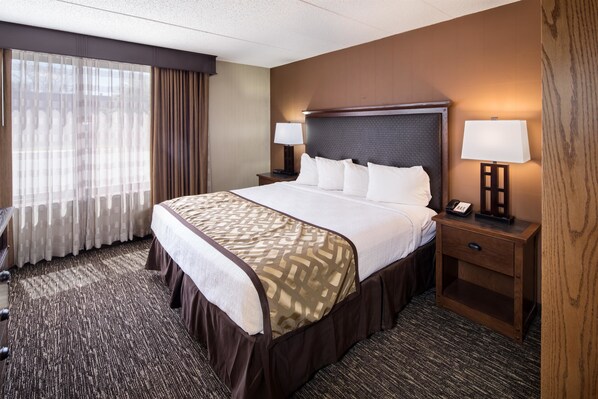 Una habitación de hotel con una cama grande, dos mesitas de noche con lámparas, una mesita auxiliar de madera y piso alfombrado.