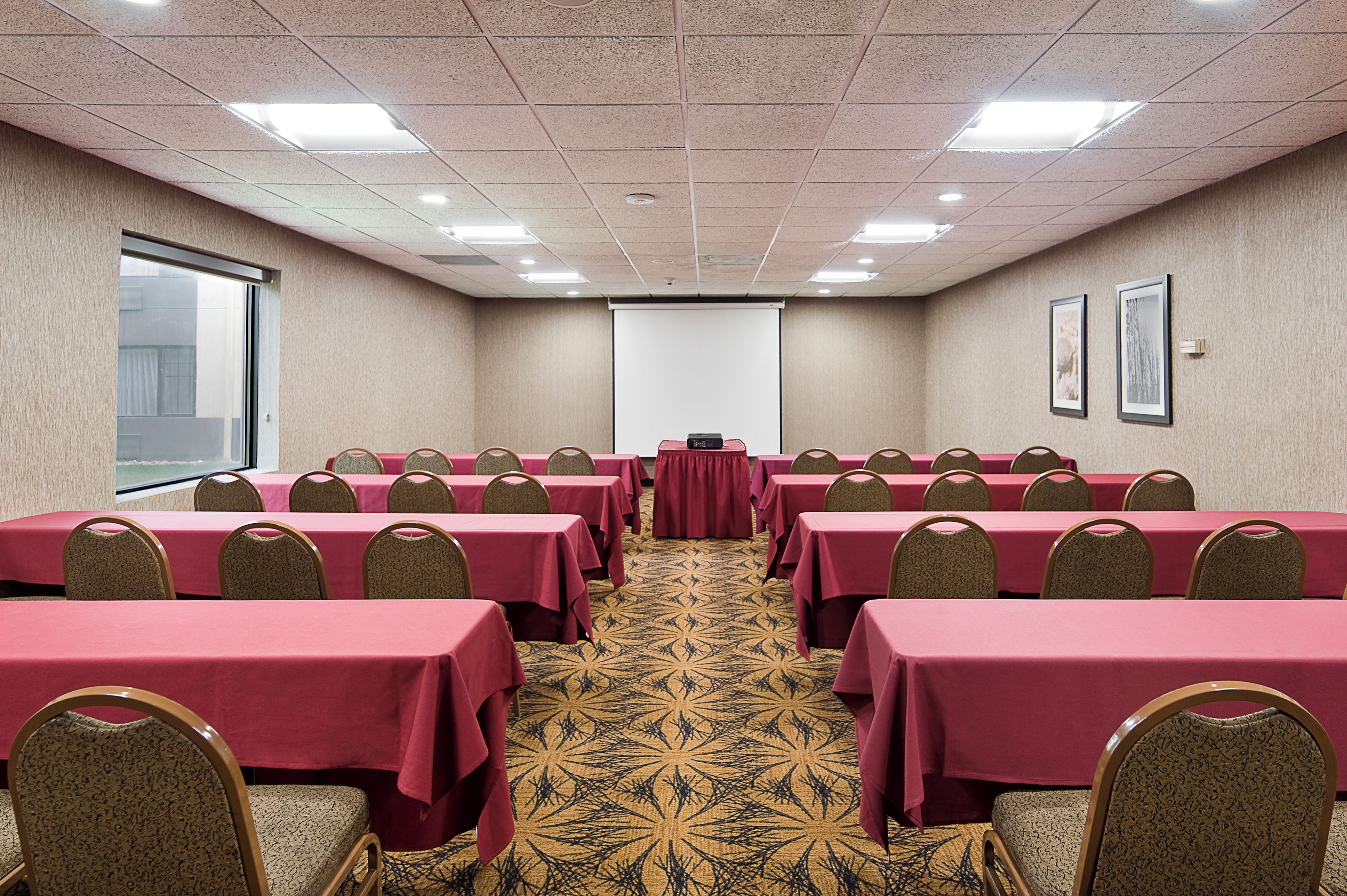 A conference room with tables and chairs, a projector screen, and a carpeted floor.