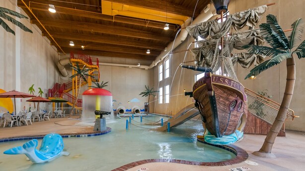 Un parque acuático interior con una zona de juegos temática de barcos, toboganes y una piscina.