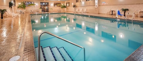 En inomhuspool med klart vatten, omgiven av solstolar och bord.