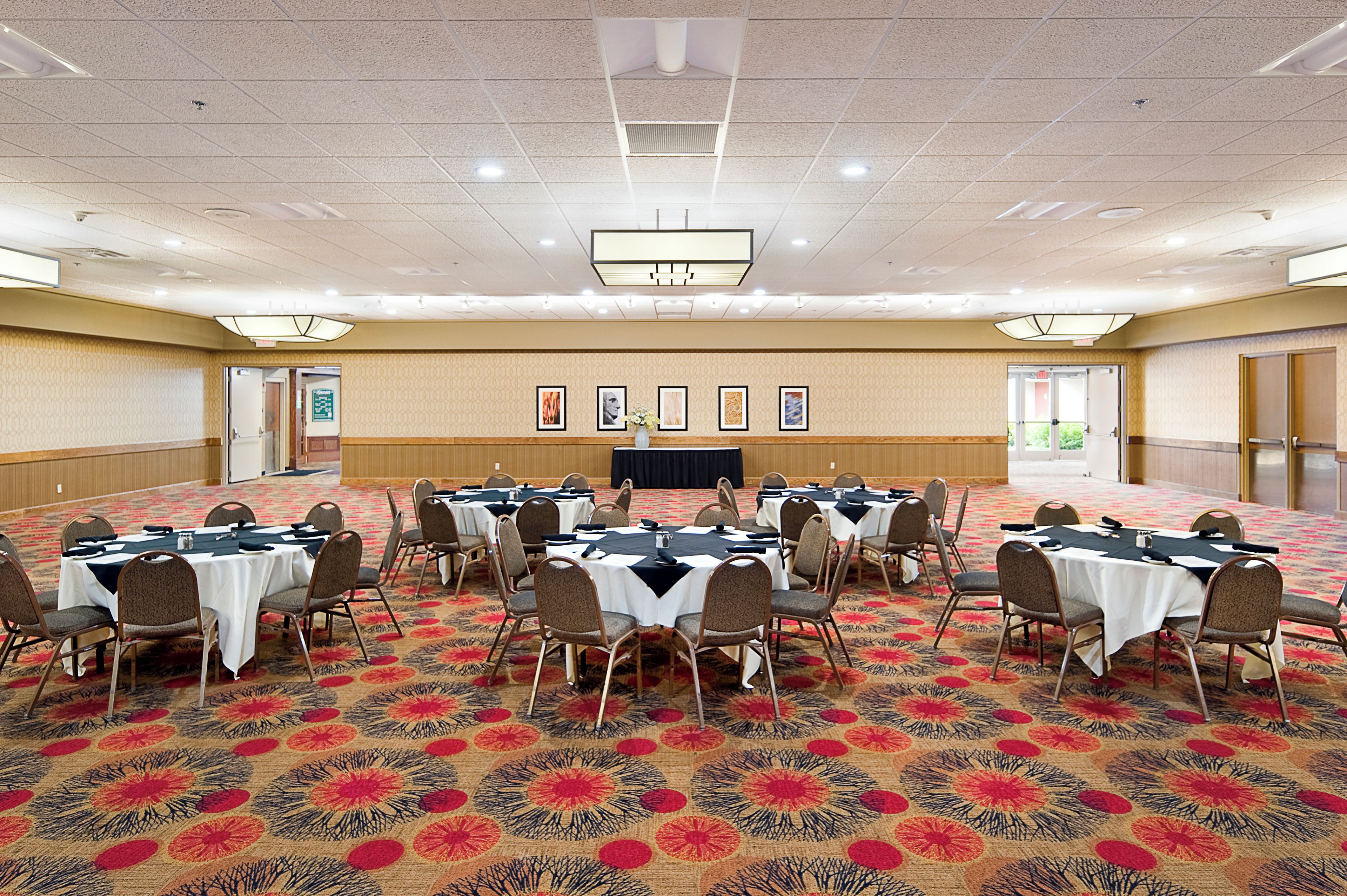 A conference room with multiple tables and chairs, a stage, and framed pictures on the wall.