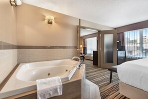 A hotel room with a large bathtub, a bed, a desk, and a view of the city through large windows. - Best Western Plus Calgary Centre Inn (Calgary)