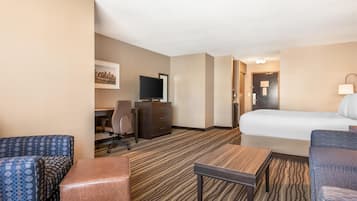A hotel room with a bed, a desk with a chair, a television, and a sofa.