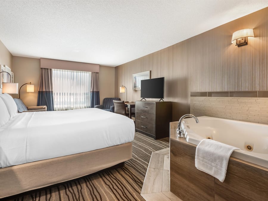 Habitación de hotel con una cama grande, baño independiente con bañera, escritorio y televisión.