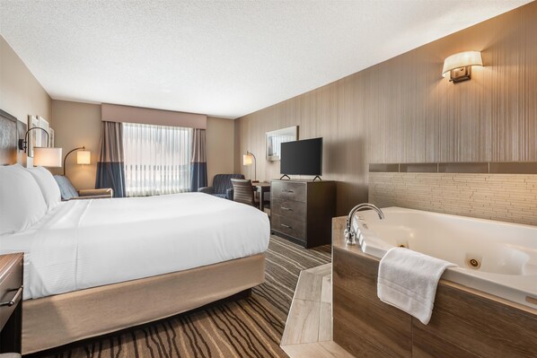 Habitación de hotel con una cama grande, baño independiente con bañera, escritorio y televisión.