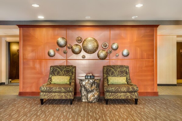 Un vestíbulo con dos sillones estampados, una mesa central y una pared decorada con platos.