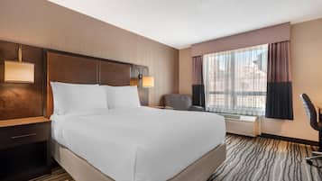 A hotel room with a large bed, two bedside lamps, a chair, a desk, and a large window with curtains.