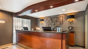 A reception desk with a modern design, featuring a wooden finish and a glass top. There are two wall-mounted lamps with circular designs, and a sign indicating the hotel's name and services. - Best Western Plus Calgary Centre Inn (Calgary)