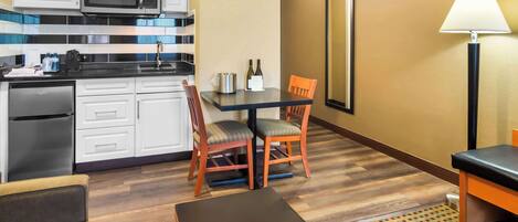 Habitación de hotel compacta con kitchenette, zona de comedor con dos sillas, una mesa y una lámpara.