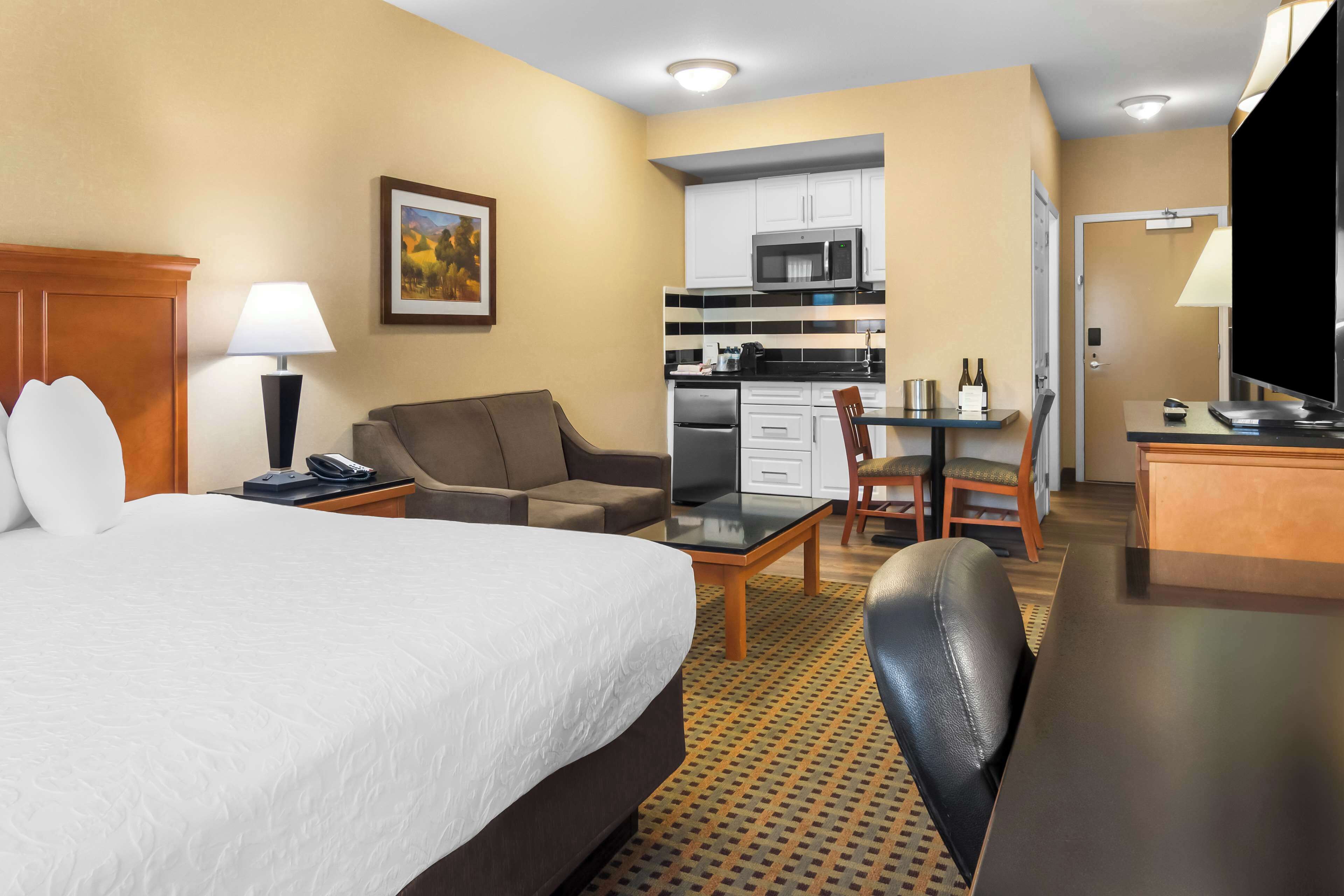 Ein Hotelzimmer mit Bett, Schreibtisch, Stuhl, Sofa, Küchenzeile und Fernseher.