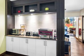 A kitchen with white cabinets, a microwave, toaster, and a red appliance for making pancakes.