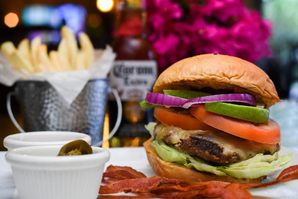 Hamburguesa con lechuga, tomate y cebolla, acompañada de papas fritas y un recipiente pequeño de salsa.