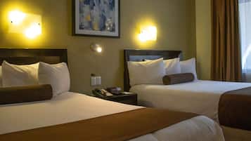 A hotel room with two beds, each with white linens and brown headboards. There are wall-mounted light fixtures on either side of the beds, and a painting above the left bed.