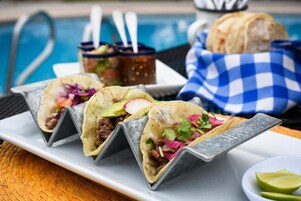 Tres tacos sobre un plato blanco, una canasta de pan y un recipiente pequeño con salsas.