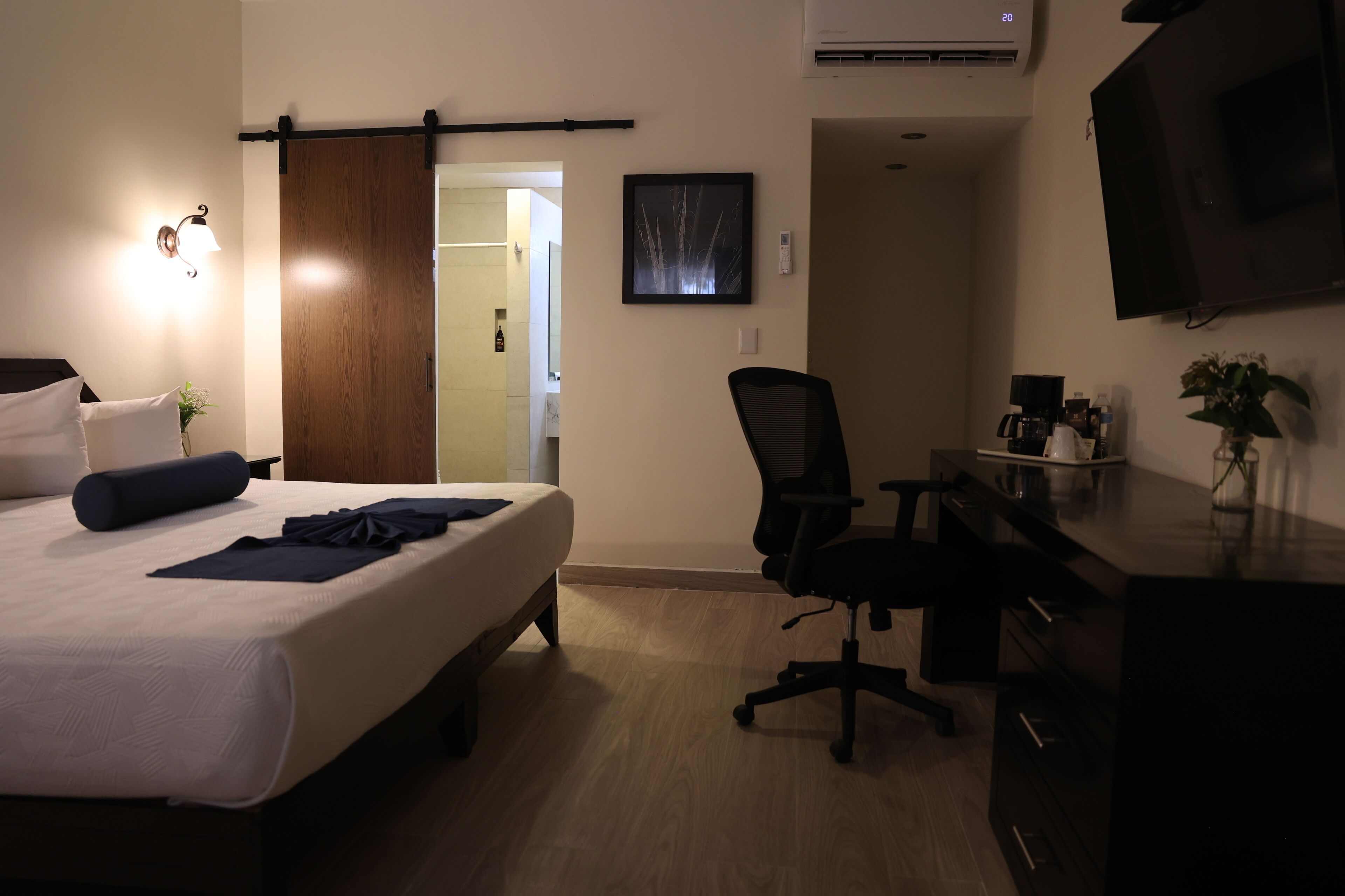 A hotel room with a bed, a desk, a chair, a TV, and a sliding door to the bathroom.