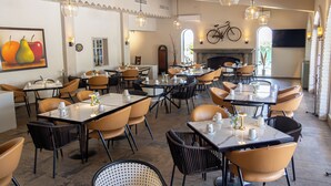 A restaurant with multiple tables and chairs, a fireplace, and a bicycle mounted on the wall. - Hotel del Rio (Navojoa)