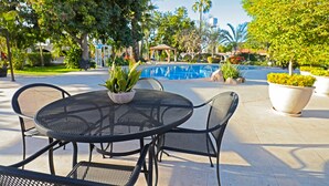 A patio area with a round metal table and chairs, a potted plant, and a view of a pool and gazebo. - Hotel del Rio (Navojoa)