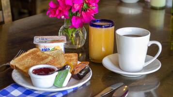 A breakfast setting with toast, jam, butter, a glass of orange juice, a cup of coffee, and a vase of flowers.