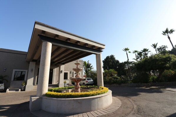 A building with a covered entrance, a fountain, and a landscaped garden. - Hotel del Rio (Navojoa)