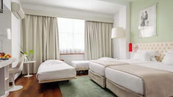 A hotel room with two beds, a desk with a chair, a small table with a vase of flowers, and a window with curtains.