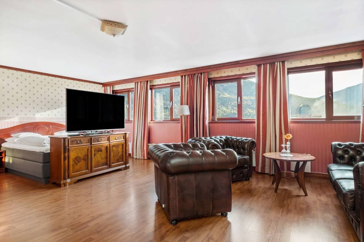 A spacious room with a large flat-screen TV, leather sofas, a wooden cabinet, and a small round table.