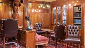 Una biblioteca con paneles de madera, sillones de cuero, un sofá rojo y una araña.