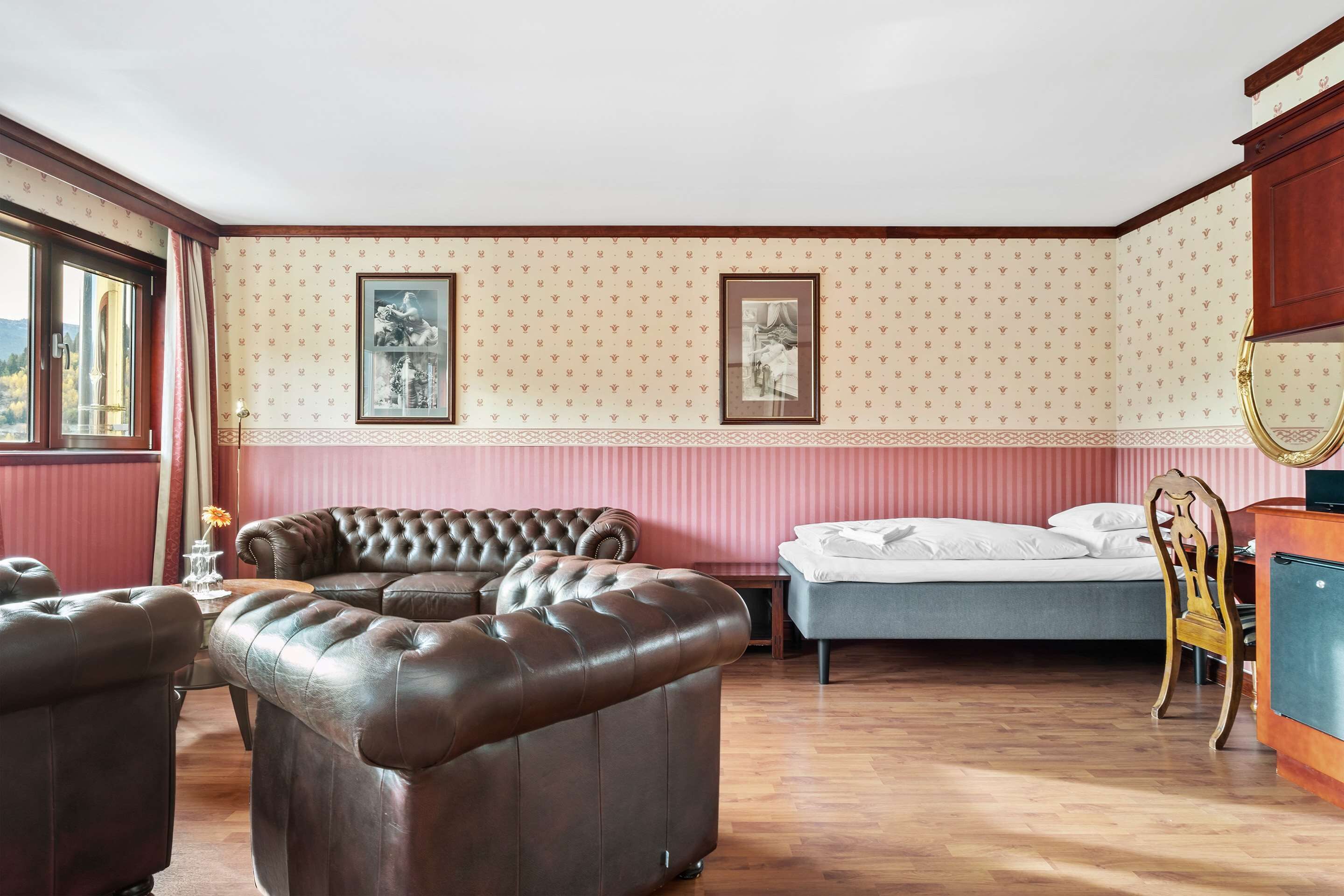 A room with a large brown leather sofa, a bed, and a wooden dresser.
