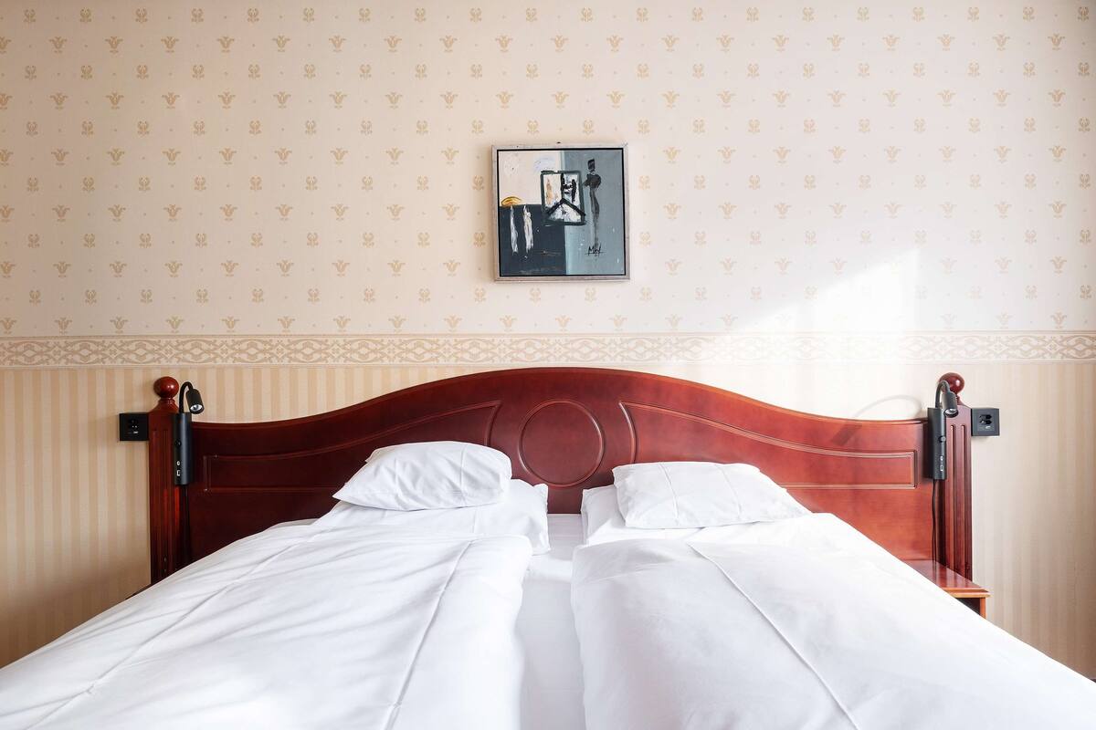 Un lit bien fait, avec du linge de lit blanc, une tête de lit en bois et une œuvre d’art encadrée au-dessus.