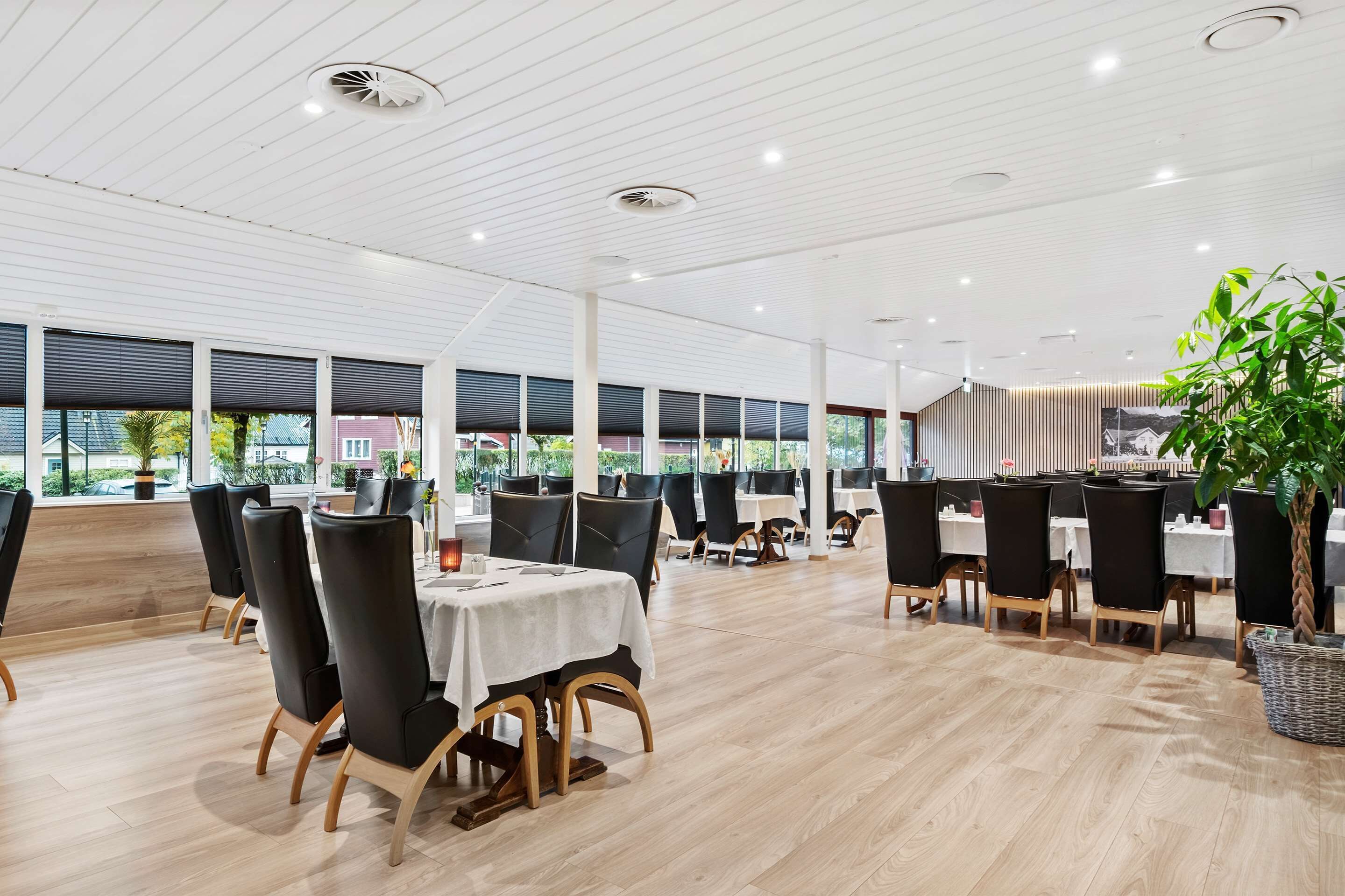 Un restaurante espacioso con techos altos, ventanas amplias y sillas negras modernas.