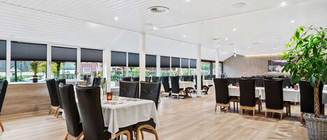 Un restaurante espacioso con techos altos, ventanas amplias y sillas negras modernas.