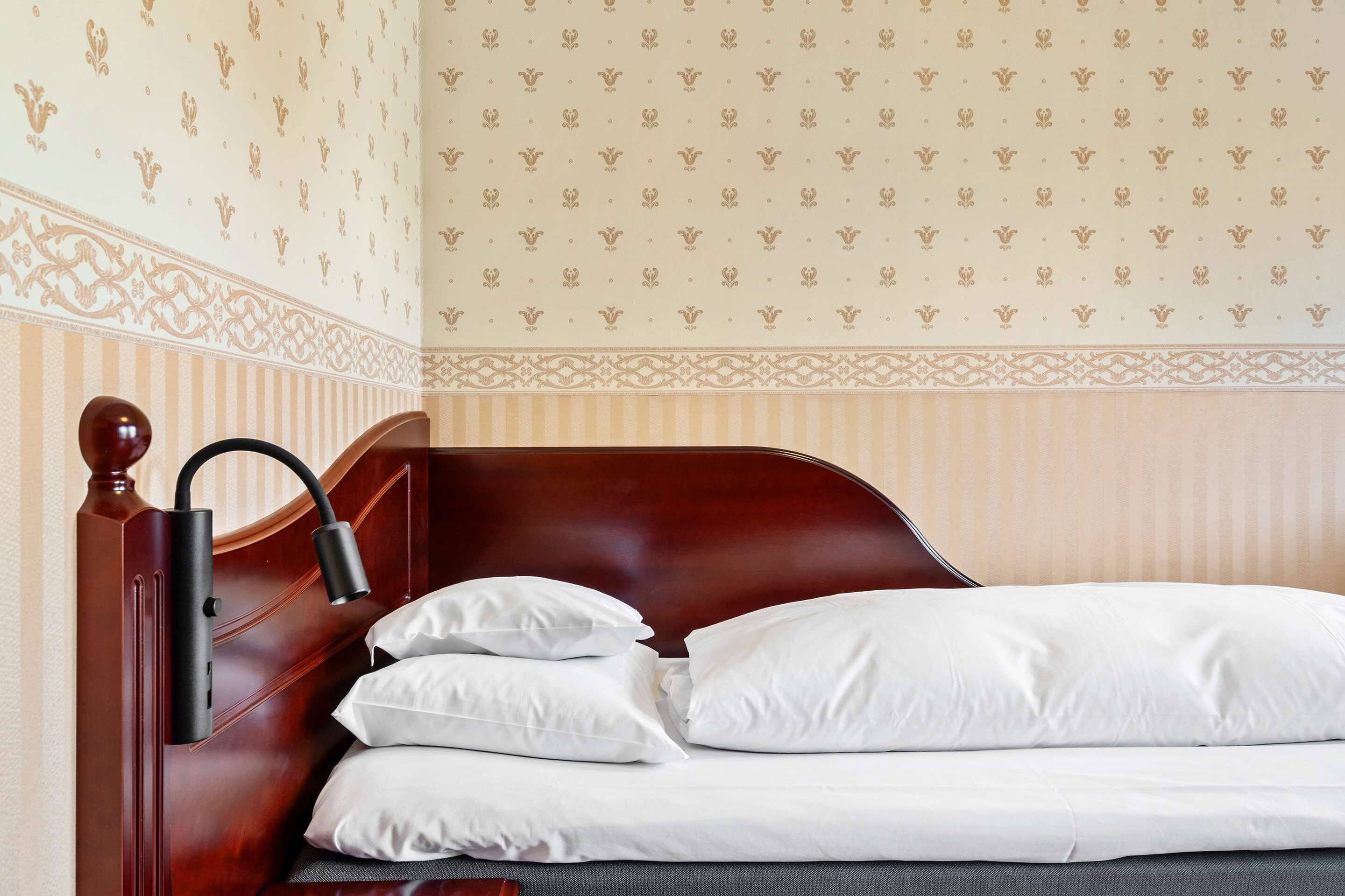 Un lit bien fait, avec du linge de lit blanc et une tête de lit en bois foncé.
