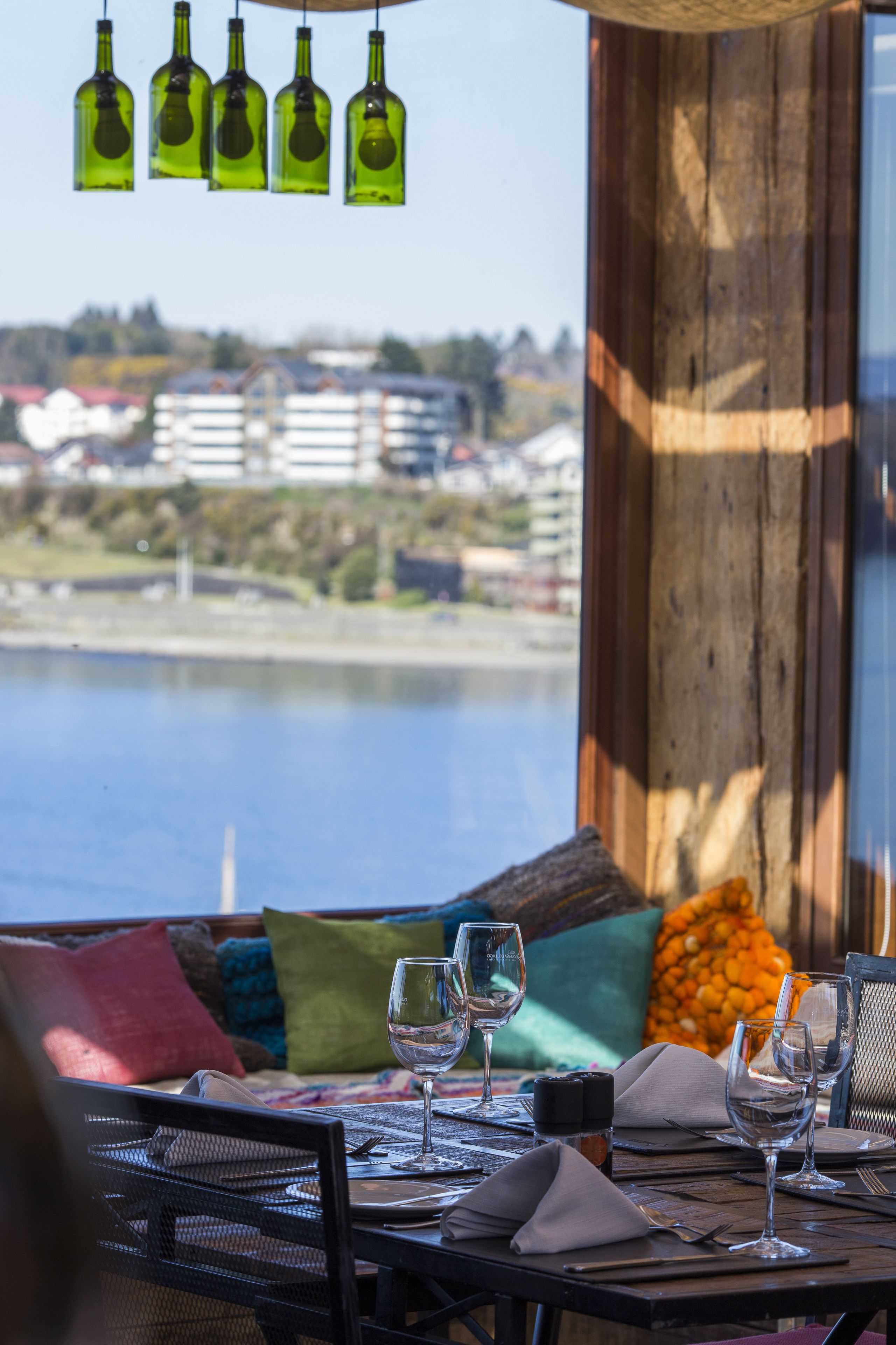 A dining table set with wine glasses, plates, and cutlery, overlooking a body of water with buildings in the background.