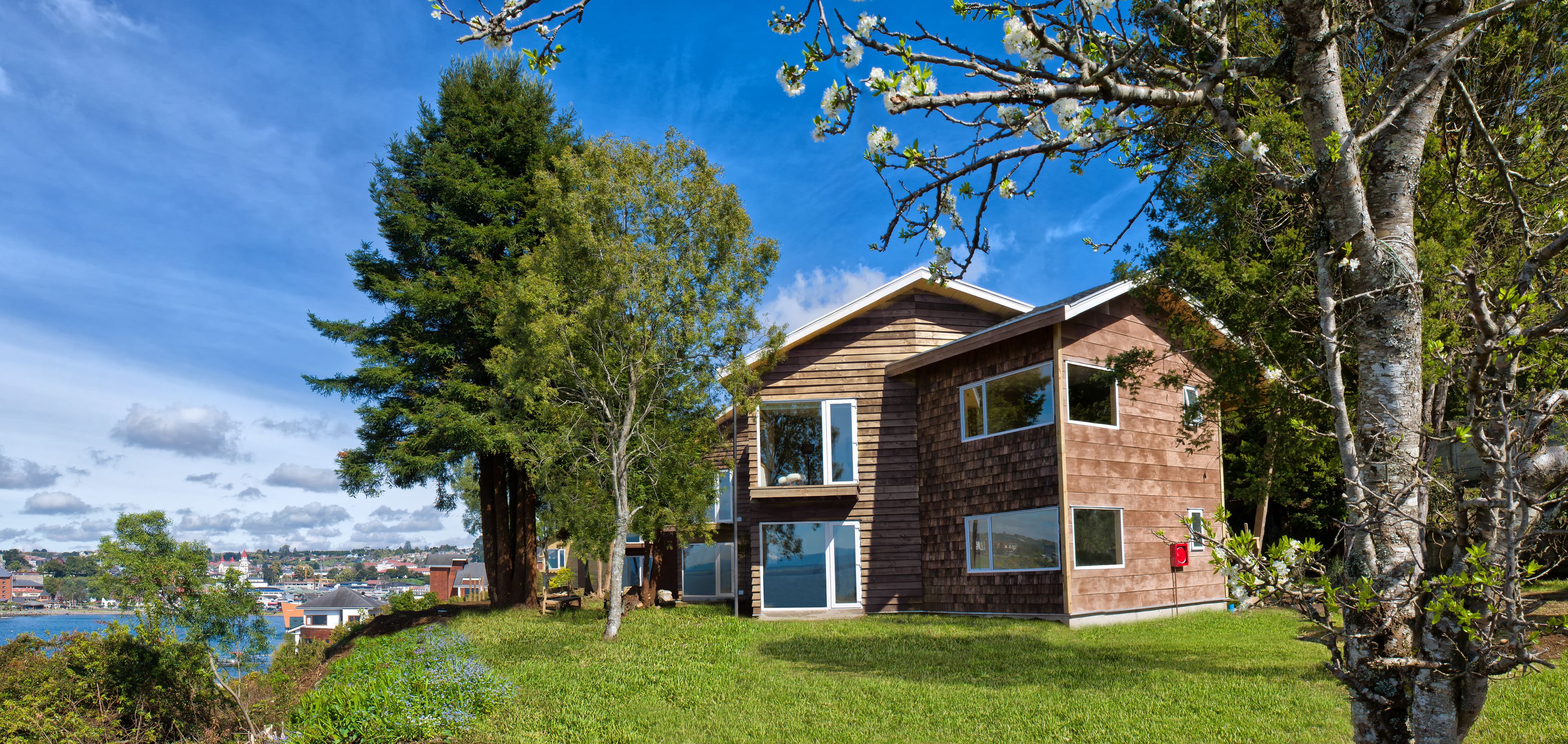 A modern two-story house with large windows and a view of a lake.