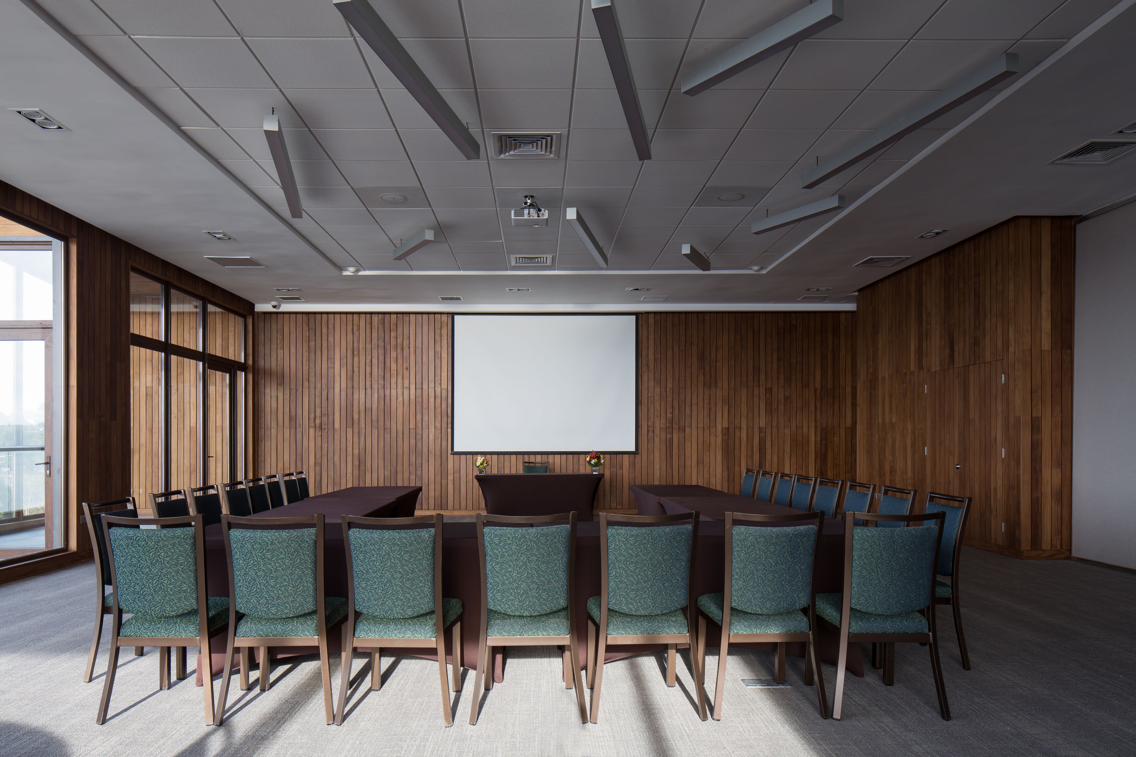 A conference room with a large table, chairs, a projector screen, and wooden panel walls.