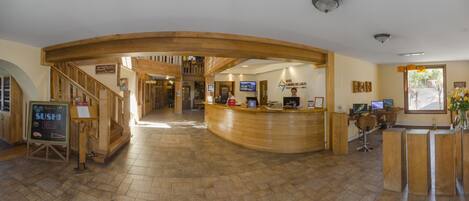 A hotel lobby with a reception desk, a sushi bar sign, and a staircase leading to another floor.